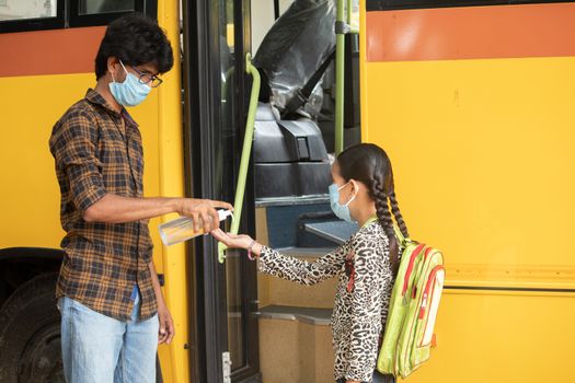 Teacher Providing hand sanitizer to students before going or getting inside the school bus while maintaining social distance as coronavirus or covid-19 safety measures