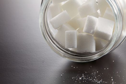 White lump sugar in a glass jar on a gray background, sweet sugar in ware with a glass opened, nobody.