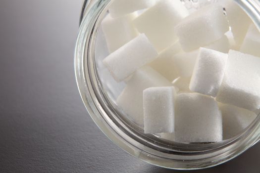 White lump sugar in a glass jar on a gray background, sweet sugar in ware with a glass opened, nobody.