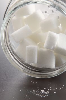 White lump sugar in a glass jar on a gray background, sweet sugar in ware with a glass opened, nobody.