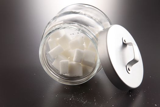 White lump sugar in a glass jar on a gray background, sweet sugar in ware with a glass opened, nobody.