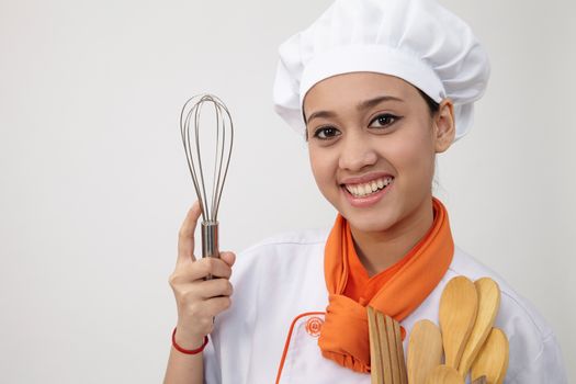 Portrait of a Indian woman with chef uniform holding whisk and spatula