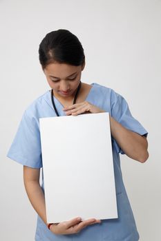 Nurse showing medical sign billboard standing, Young smiling woman nurse or doctor in scrubs showing empty blank sign board with copy space. Indian model isolated on white background