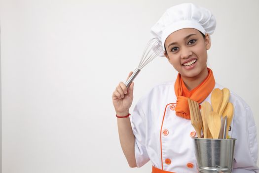 Portrait of a Indian woman with chef uniform holding whisk and spatula