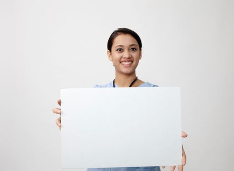 Nurse showing medical sign billboard standing, Young smiling woman nurse or doctor in scrubs showing empty blank sign board with copy space. Indian model isolated on white background