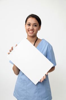 Nurse showing medical sign billboard standing, Young smiling woman nurse or doctor in scrubs showing empty blank sign board with copy space. Indian model isolated on white background