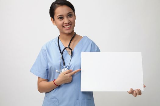 Nurse showing medical sign billboard standing, Young smiling woman nurse or doctor in scrubs showing empty blank sign board with copy space. Indian model isolated on white background