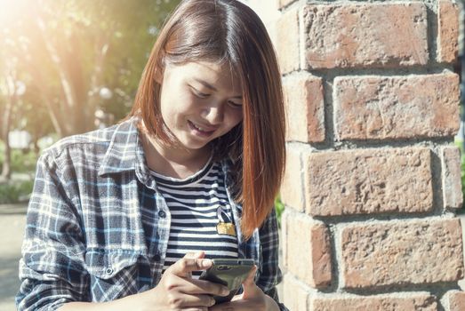 smiling woman text messaging on mobile phone in park
