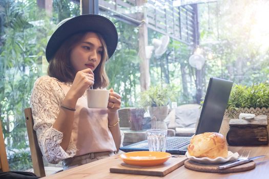 Asian women holding coffee cup looking laptop in cafe