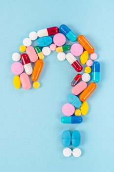 A question mark from laid out of medicine pills on blue background.