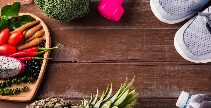 Top view of various fresh organic fruit and vegetable in heart plate and sports shoes, dumbbell and water, studio shot on wooden gym table, Healthy diet vegetarian food concept, World food day