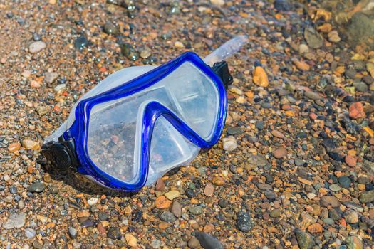 Lost diving goggles lie on a river pebble on the shore. Diving accessories