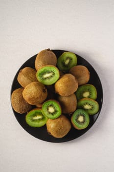 Kiwi fruits half sliced in black plate on vibrant plain white background, copy space, top view