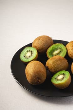 Kiwi fruits half sliced in black plate on vibrant plain white background, copy space, angle view