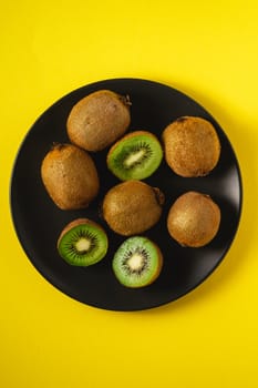 Kiwi fruits half sliced in black plate on yellow background, top view
