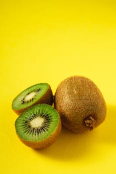 Kiwi fruits half sliced on vibrant plain yellow background, copy space, angle view