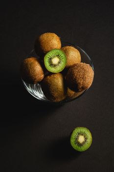 Kiwi fruits half sliced in glass bowl on dark background, angle view