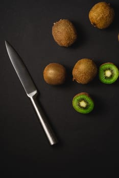 Kiwi fruits half sliced with kitchen knife on dark background