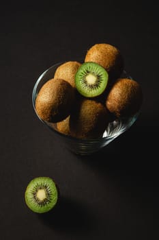 Kiwi fruits half sliced in glass bowl on dark background, angle view