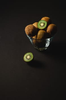 Kiwi fruits half sliced in glass bowl on dark background, angle view