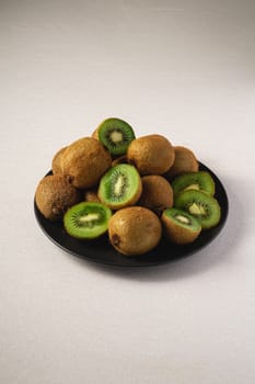 Kiwi fruits half sliced in black plate on vibrant plain white background, copy space, angle view