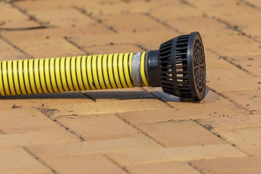 Yellow irrigation suction hose with a black filter lying on brown bricks in the sunshine