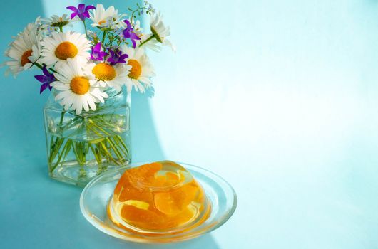 Breakfast jelly with tangerine slices and a bunch of daisies on a blue background.