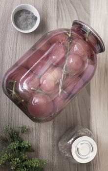 Home preservation: a large glass jar with red ripe pickled tomatoes, closed with a metal lid, next to spices and herbs. Top view, close-up.