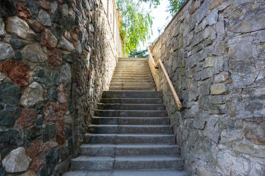 A stone staircase with a railing leading up.Summer day.