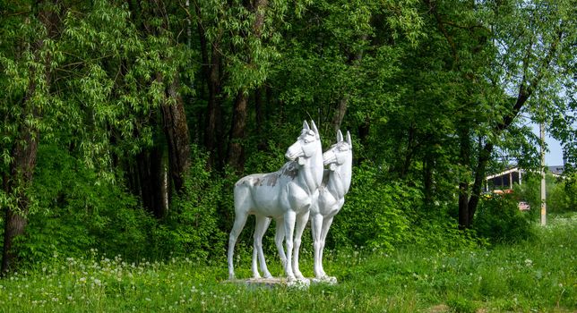 Sculpture of two white moose on the background of a green forest, on the outskirts of a provincial town