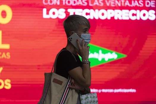 Zaragoza, Spain - August 18, 2020: A woman talks throughout the smartphone, with face mask, due to the coronavirus pandemic, in the central area of Zaragoza.