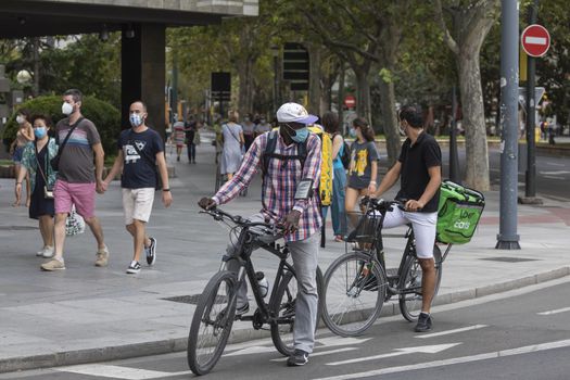 Zaragoza, Spain - August 18, 2020: Glovo and Uber Eats riders working with face mask, due to the coronavirus pandemic, in the central area of Zaragoza.