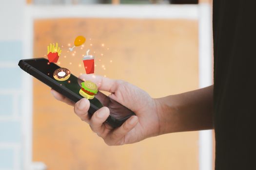Food delivery concept. Hand holding black smartphone or mobile phone and food cartoon icon to search for lunch or dinner. Online food in new normal.