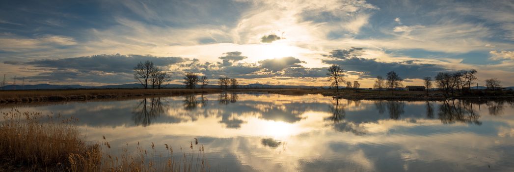 Picturesque sunset over the river. Multicolored clouds are reflected in the water.