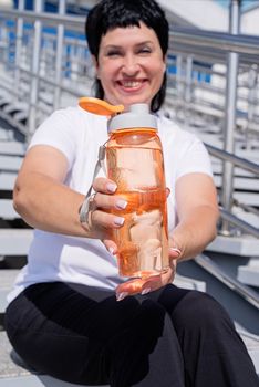 Sport and fitness. Senior sport. Active seniors. Smiling senior woman drinking water after workout outdoors on urban background