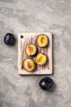 Fresh ripe plum fruits whole and sliced on wooden cutting board, stone concrete background, top view