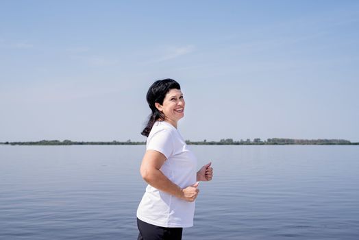 Sport and fitness. Senior sport. Active seniors. Active senior woman jogging near the riverside