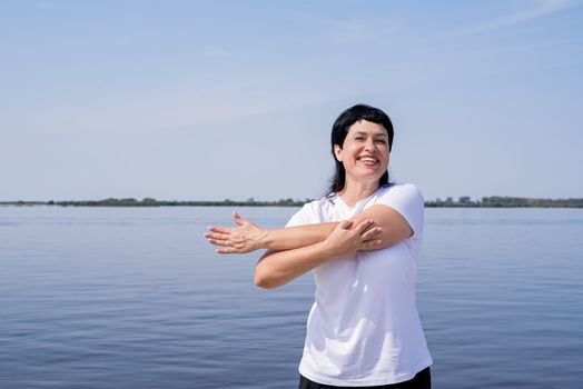 Sport and fitness. Senior sport. Active seniors. Active and happy senior woman doing stretching near the riverside