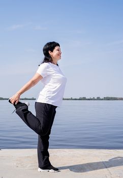 Sport and fitness. Senior sport. Active seniors. Active and happy senior woman doing stretching near the riverside