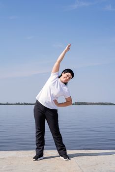 Sport and fitness. Senior sport. Active seniors. Active and happy senior woman doing stretching near the riverside