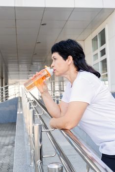 Sport and fitness. Senior sport. Active seniors. Smiling senior woman drinking water after workout outdoors on urban background