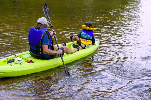 Grandfather and grandson sit in a kayak to sail along the lake along the rocks in a kayak