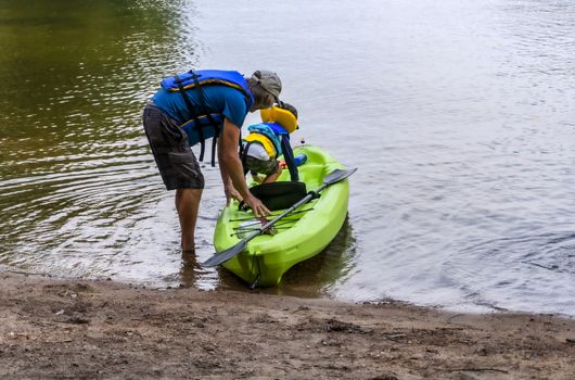 Grandfather and grandson sit in a kayak to sail along the lake along the rocks in a kayak