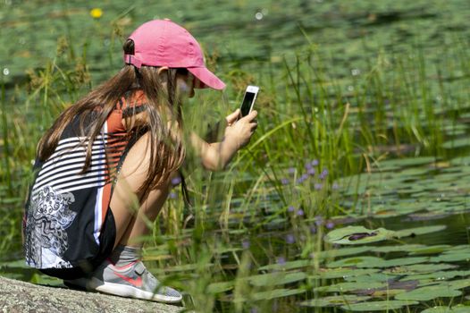 The girl saw a snake on the lake and is trying to photograph it