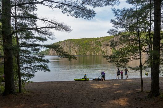 The boy brought an oar and waits for his grandfather on the shore near the kayak to swim together to the rocks in a kayak