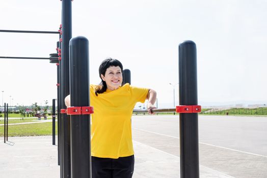 Sport and fitness. Senior sport. Active seniors. Smiling senior woman doing reverse push ups outdoors on the sports ground bars