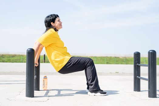 Sport and fitness. Senior sport. Active seniors. Smiling senior woman doing reverse push ups outdoors on the sports ground bars