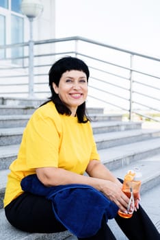 Sport and fitness. Senior sport. Active seniors. Smiling senior woman drinking water after workout outdoors on urban background