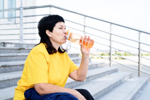 Sport and fitness. Senior sport. Active seniors. Smiling senior woman drinking water after workout outdoors on urban background