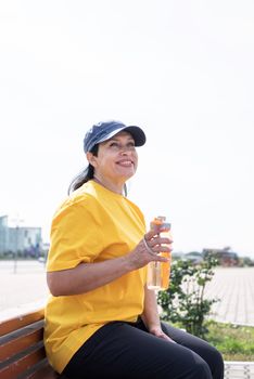 Sport and fitness. Senior sport. Active seniors. Smiling senior woman drinking water after workout outdoors on the sports ground